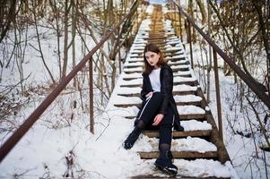 modèle brune à longues jambes à la mode dans un long manteau noir posé en plein air le jour de l'hiver. photo