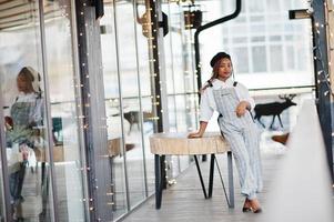 femme afro-américaine en salopette et béret posé sur une terrasse extérieure avec guirlande de décorations de noël. photo