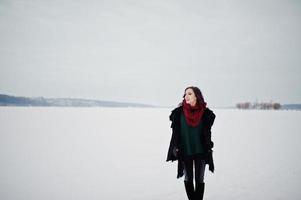 fille brune en chandail vert et écharpe rouge lac gelé en plein air le soir de la journée d'hiver. photo