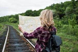 portrait d'une jolie fille blonde en chemise tartan marchant sur le chemin de fer avec une carte dans les mains. photo