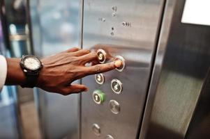 photo en gros plan de la main d'un homme afro-américain avec des montres à l'élévateur ou à l'ascenseur moderne, en appuyant sur le bouton.