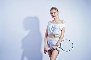 incroyable corps sexy brune caucasienne fille posant au studio sur fond blanc sur un short et un haut avec une raquette de badminton. photo