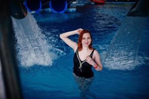 fille sexy aux cheveux rouges en maillot de bain noir se reposant dans la piscine du parc aquatique. photo