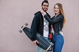 cool couple multiracial posant contre un mur rose avec longboard. photo