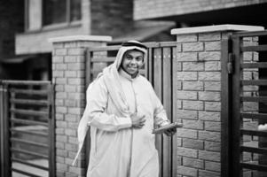 homme arabe du moyen-orient posé dans la rue contre un bâtiment moderne avec une tablette à portée de main. photo