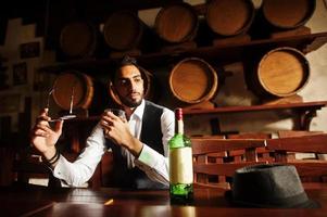 bel homme arabe bien habillé avec un verre de whisky et de cigare posé au pub. photo