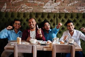 groupe de quatre hommes sud-asiatiques posés lors d'une réunion d'affaires au café. les indiens regardent la télévision et encouragent leur équipe préférée. photo