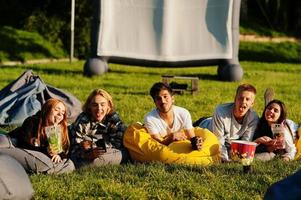 jeune groupe multiethnique de personnes regardant un film au pouf dans un cinéma en plein air. photo