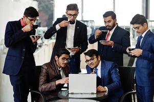 groupe de six hommes d'affaires indiens en costumes assis au bureau sur un café regardant un ordinateur portable et buvant du café. photo