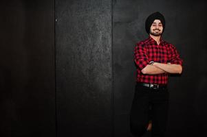 homme indien en chemise à carreaux et turban noir sur fond sombre. photo