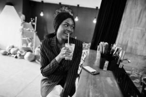 femme d'affaires afro-américaine buvant de la limonade cocktail au café au bar. fille noire se reposant avec un téléphone portable. photo