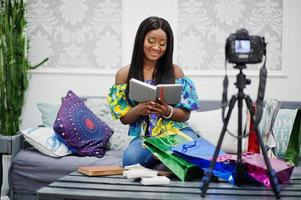 jolie femme afro-américaine réalisant une vidéo pour son blog à l'aide d'un appareil photo numérique monté sur trépied. jeune blogueuse ou vlogger à la caméra.