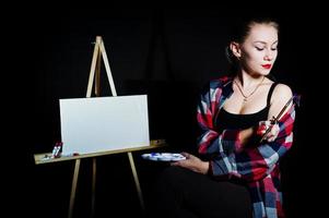 belle femme artiste peintre avec pinceaux et toile à l'huile posant en studio isolé sur noir. photo
