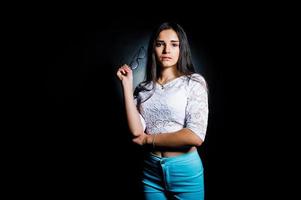 portrait d'une jolie jeune femme en haut blanc et pantalon bleu posant avec ses lunettes dans le noir. photo