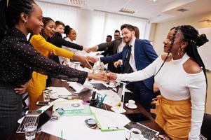 bonne affaire. équipe commerciale multiraciale s'adressant à une réunion autour d'une table de réunion et se serrant la main. photo