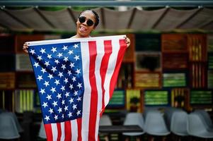 élégante femme afro-américaine à lunettes de soleil posée en plein air avec le drapeau américain. photo