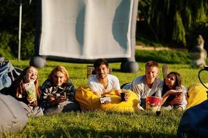 jeune groupe multiethnique de personnes regardant un film au pouf dans un cinéma en plein air. photo