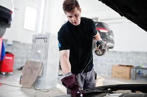 thème de la réparation et de l'entretien des voitures. mécanicien en uniforme travaillant dans le service automobile, vérifiant le moteur. photo