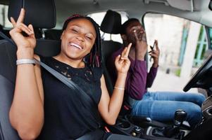 beau jeune couple afro-américain assis sur les sièges passagers avant tandis que bel homme conduisant une voiture. écouter de la musique et de la danse. photo