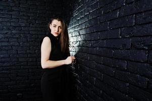 portrait d'une belle fille brune en combinaison noire dans le studio à côté du mur de briques. photo