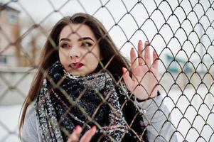 gros plan le portrait d'une jeune fille brune en écharpe contre la cage. photo