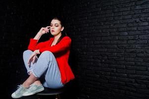 fille brune élégante sur une veste rouge contre le mur de briques noires du studio. photo