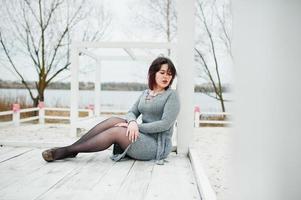 portrait de jeune fille brune en robe grise assis à la construction en bois blanc. photo