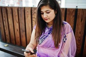 fille hindoue indienne au sari violet traditionnel assis à la table du café avec un téléphone portable à portée de main. photo