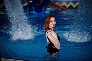 fille sexy aux cheveux rouges en maillot de bain noir se reposant dans la piscine du parc aquatique. photo