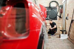 le travailleur du service automobile a mis un film anti-gravier sur une carrosserie de voiture rouge à l'atelier de détail du véhicule. protection de voiture avec des films spéciaux. photo