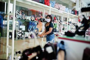 femme afro-américaine portant un masque médical de protection du visage pour la protection contre les maladies virales dans le magasin de chaussures pendant la pandémie de coronavirus. photo