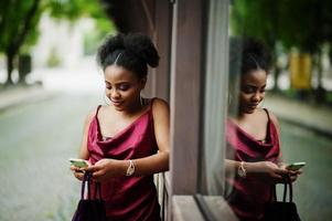 portrait d'une belle jeune femme africaine naturelle aux cheveux afro. modèle noir en robe de soie rouge avec téléphone portable. photo