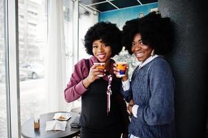 deux femmes afro-américaines aux cheveux bouclés portent des chandails avec des tasses de thé posées au café à l'intérieur. photo