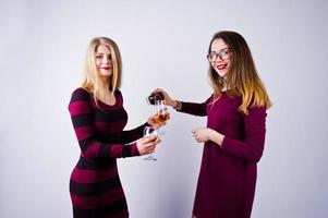 deux jolies amies en robes violettes boivent du vin mousseux ou du champagne dans le studio. photo