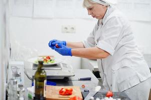 chef féminin préparant une salade dans la cuisine du restaurant italien. photo