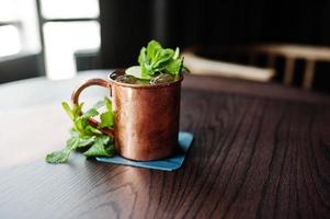 cocktail alcoolisé avec glace, menthe et citron vert dans une tasse en bronze sur table de bar. photo