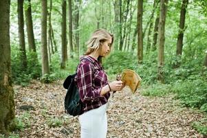 portrait d'une belle jeune femme blonde en chemise tartan tenant une carte dans la forêt. photo