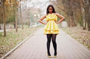 femme afro-américaine élégante en robe jaune posée contre le parc d'automne. photo