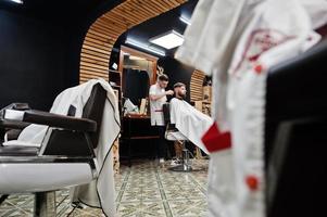 jeune homme barbu se coupe les cheveux par un coiffeur assis sur une chaise au salon de coiffure. âme de barbier. photo