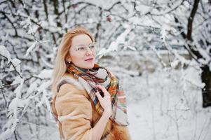 portrait d'une fille blonde à lunettes, manteau de fourrure rouge et écharpe le jour de l'hiver. photo