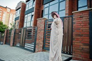 homme d'affaires arabe du moyen-orient posé dans la rue contre un bâtiment moderne avec des lunettes de soleil, parlant au téléphone mobile. photo