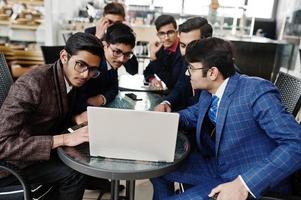 groupe de six hommes d'affaires indiens en costumes assis au bureau sur un café et regardant un ordinateur portable. photo