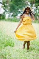 portrait d'une magnifique femme afro-américaine des années 20 en robe jaune et chapeau d'été posant sur l'herbe verte dans le parc. photo