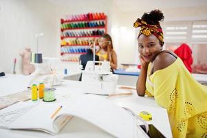 deux couturières africaines cousent des vêtements sur une machine à coudre au bureau de tailleur. filles couturières noires. photo