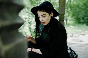 sensuelle fille fumeuse tout en noir, lèvres rouges et chapeau. goth dramatique femme fumant une cigarette mince. photo