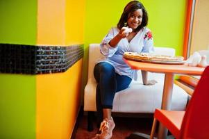 une femme africaine verse du sel à la pizza alors qu'elle est assise dans un restaurant aux couleurs vives. photo