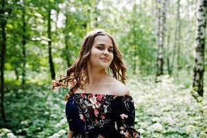 portrait d'une fabuleuse jeune fille en jolie robe avec une coiffure bouclée élégante posant dans la forêt ou le parc. photo