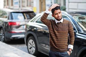 portrait d'un modèle de jeune homme indien élégant pose dans la rue contre une voiture suv. photo