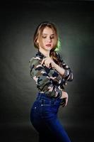 belle fille brune porte une chemise militaire et un jean, posant au studio sur fond gris. portrait de modèle de studio. photo