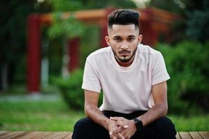 homme barbe indien élégant au t-shirt rose. modèle indien assis sur un banc de la ville. photo